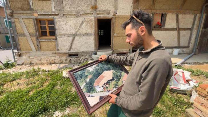 Devant sa ferme typique alsacienne en cours de rénovation, Hugo regarde une photo aérienne prise à l'époque où un enduit recouvrait les murs